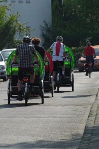 Drei Rikschafahrende in der Rückenansicht im Straßenverkehr.