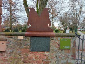 Zwei Punguine stehen Rücken an Rücken auf der Friedhofsmauer in Groß-Auheim. Die Skulptur ist ein Scherenschnitt.