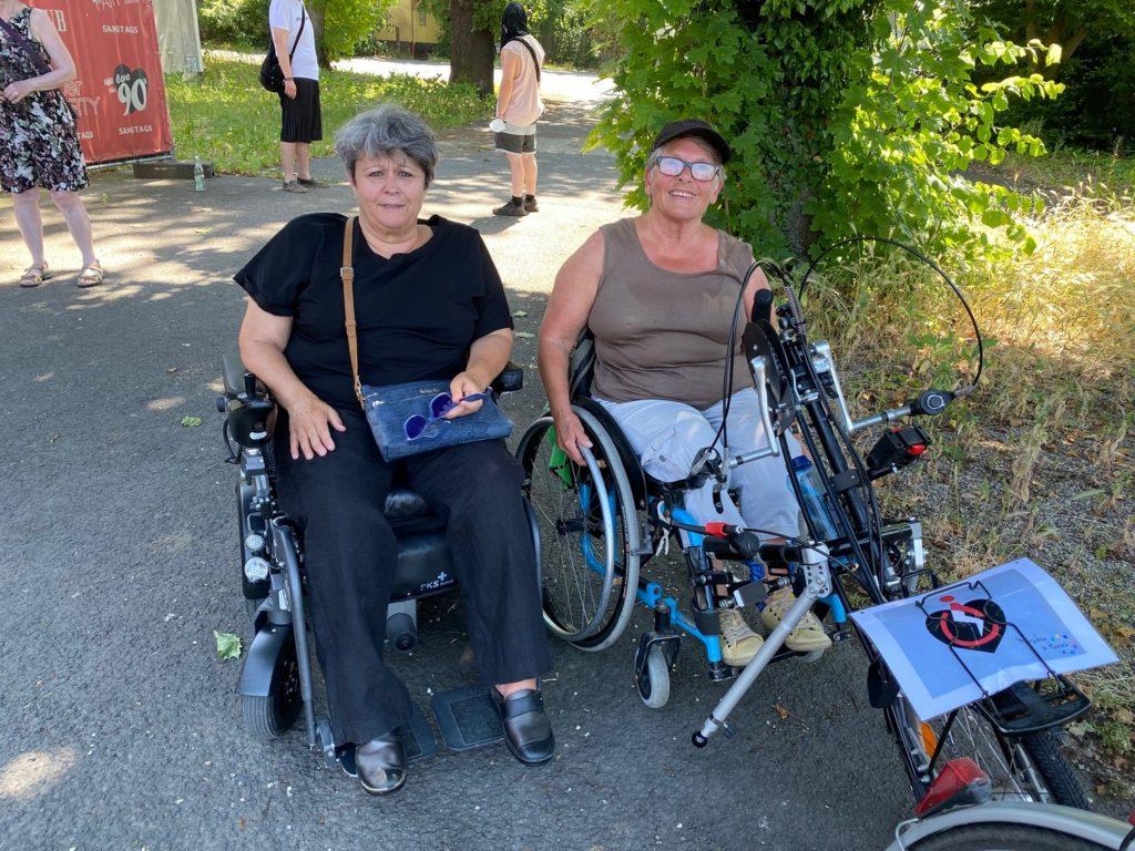 Das Bild zeigt Gaby in ihrem Elektro-Rollstuhl und Marianne mit dem Handbike.