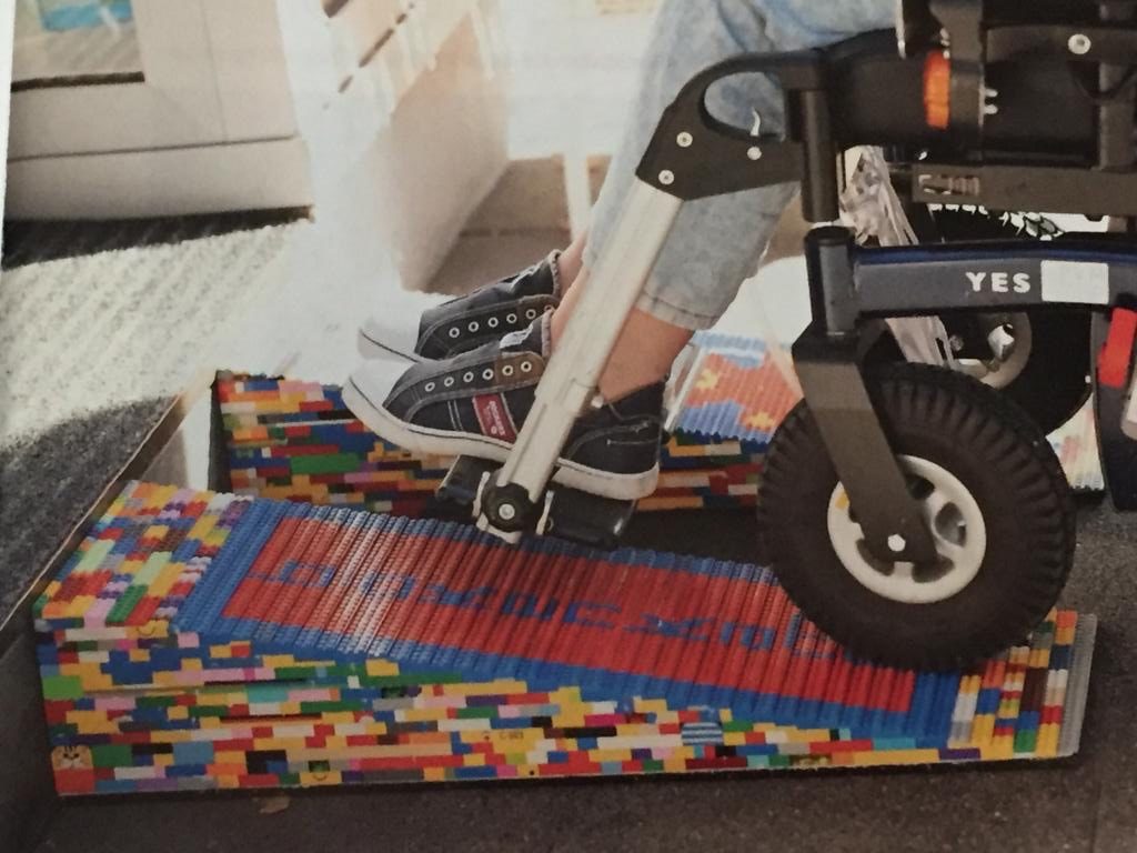 Rollstuhl fährt über eine Rampe. Die LEGO-Rampen liegen vor dem Eingang des Geschäfts.