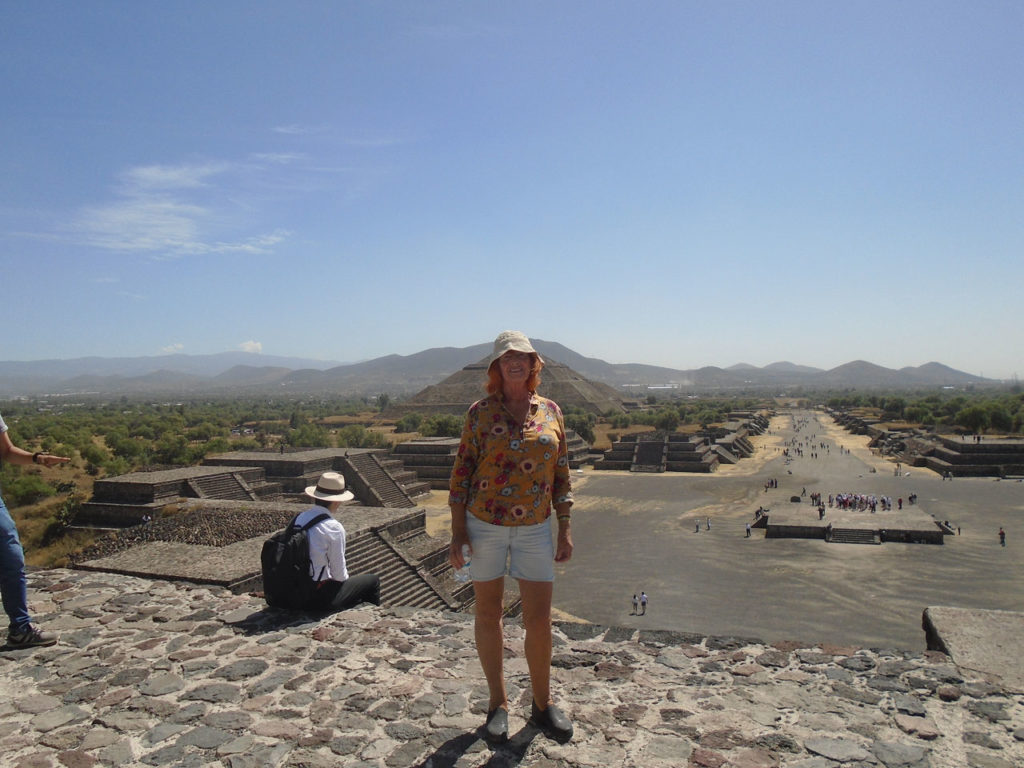 Ausflug nach Teotihuacan zu Mond- und Sonnenpyramide. Elke steht auf den Stufen der Mondpyramide genau vor der Sonnenpyramide. Die Sonne strahlt, sie trägt einen Hut.