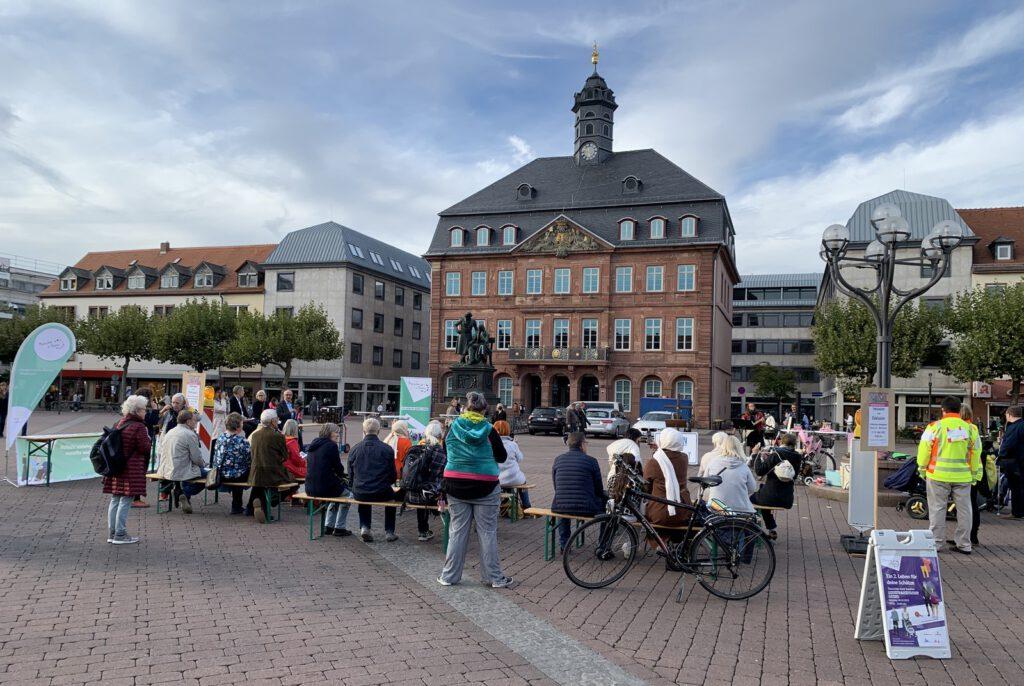 Das Bild zeigt den Marktplatz mit den Zuschauern und der Bühne. Im Hintergrund ist das alte Rathaus zu sehen. Es sind alle Sitzplätze belegt.