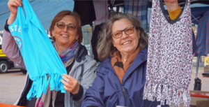 Zwei engagierte Näherinnen zeigen ihre gerade gefertigten Einkaufstaschen aus alten Kleidungsstücken. Die eine ist blau, die andere lila-weiß.