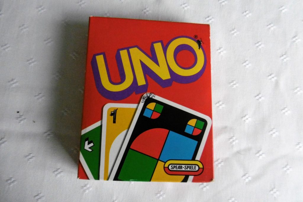 Die Verpackung vom Spiel UNO. Ein roter Karton mit drei Beispielkarten.