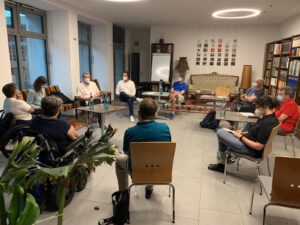 2021: Austausch mit Hanau Infra Struktur Service. Mehrere Personen sitzen im AJOKI im Kreis, darunter zwei Frauen im Rollstuhl. Alle tragen Corona-Masken.