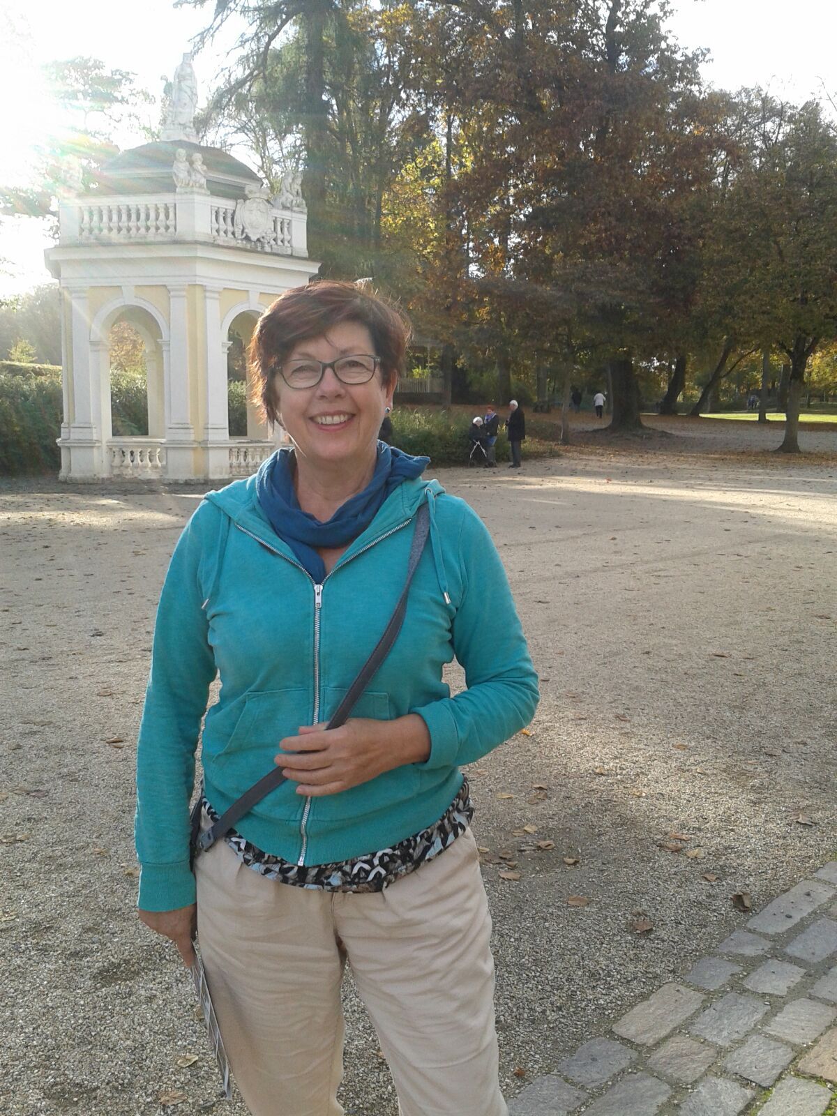 Birgitt stett mit hellblauem Pullover an einem schönen Tag im Park.