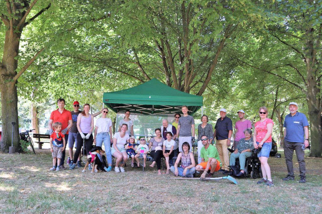 Gruppenfoto vor unserem grünen Menschen in Hanau Zelt und einem großen Baum. Circa 30 Menschen sind zu sehen.