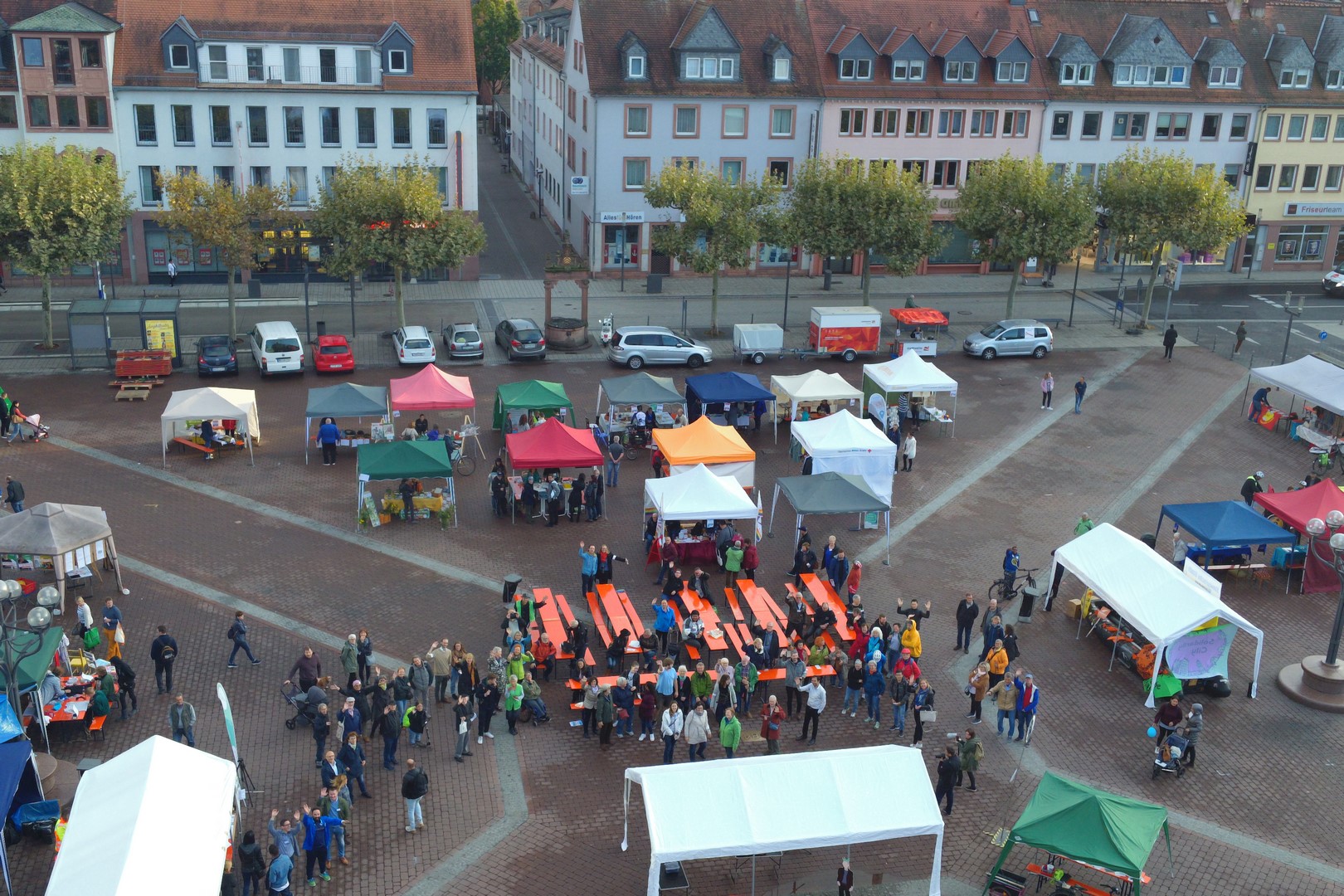 Ein Bild von oben vom 1. Demokratie-RAUM in Hanau. Man sieht die bunten Mitmach-Zelte und die Menschen, die sich zum Input auf dem Marktplatz versammeln.