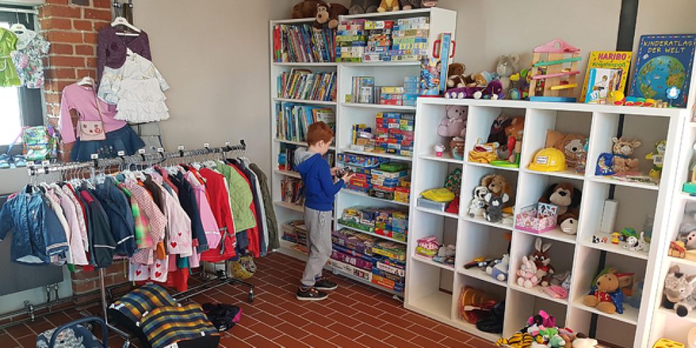 DRK Kinderkleiderladen. Man sieht auf dem Bild ein Regal mit vielen Kinderspielsachen und ein kleines Kind, was davor steht.