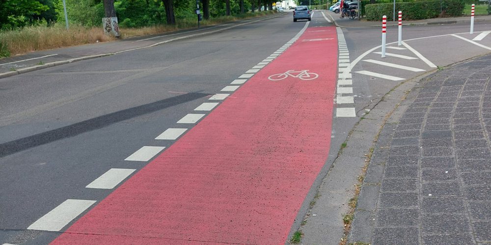 Ein rot markierter Radweg ändert nicht seine Richtung, Der Autoverkehr muss beim Abbiegen den Radweg kreuzen.