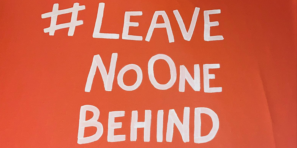 Auf orangefarbenen Stoff wurde mit weißer Farbe folgendes geschrieben#Leave no one behind