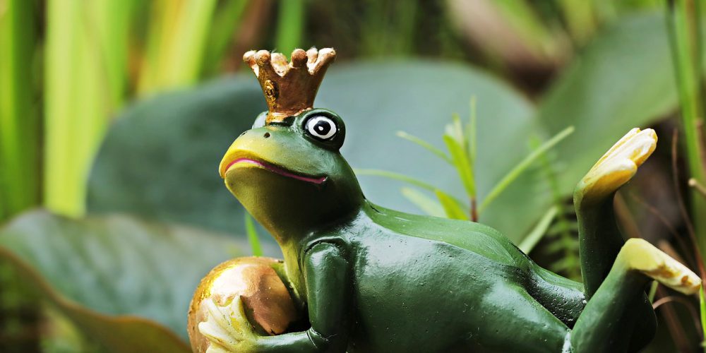 Das Bild zeigt einen Frosch mit einer Krone, der einen goldenden Ball hält.