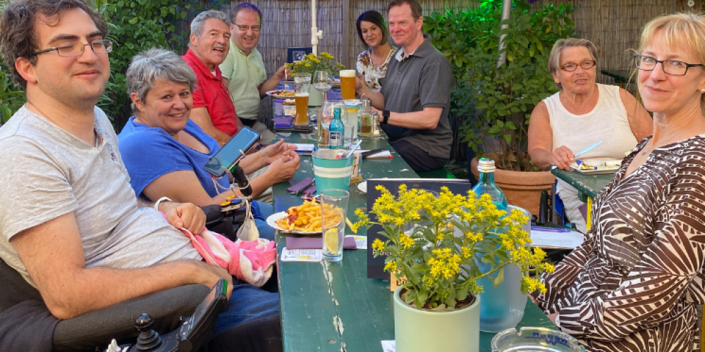 Checker Team sitzt an einer gemeinsam an einer Bierzeltgarnitur mit Essen, Blumen und Trinken auf dem Tisch. Alle lachen in die Kamera.