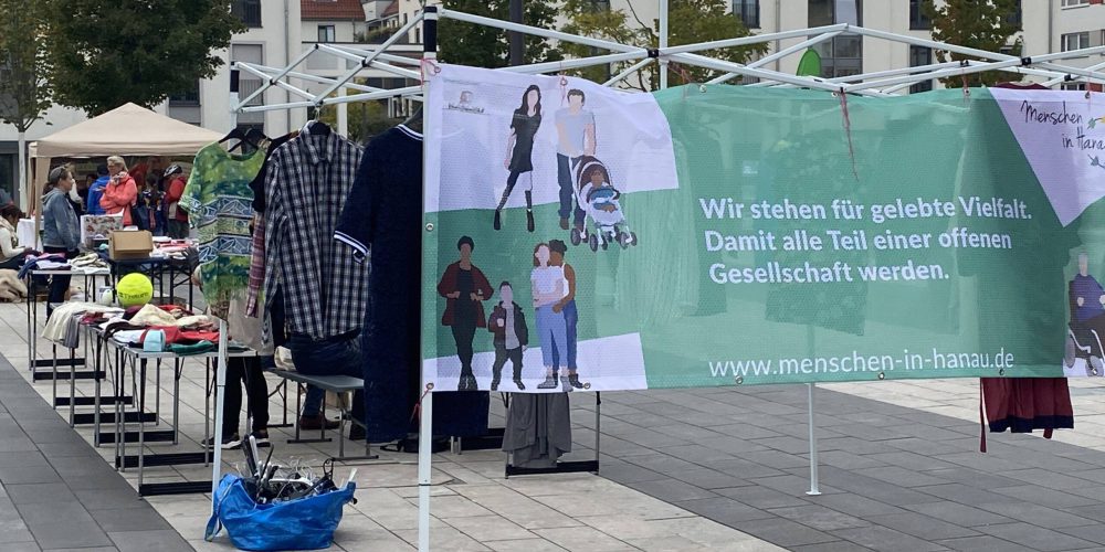Grüner Menschen in Hanau Banner mit den dahinterliegende Tauschständen