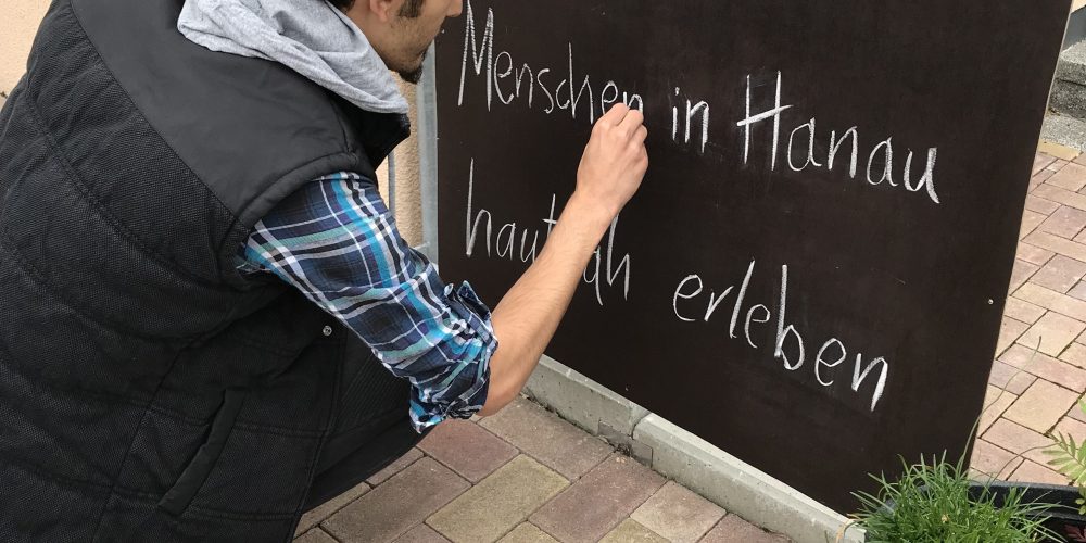 Mulham schreibt mit Kreide auf eine Tafel: Heute : Menschen in Hanau hautnah erleben