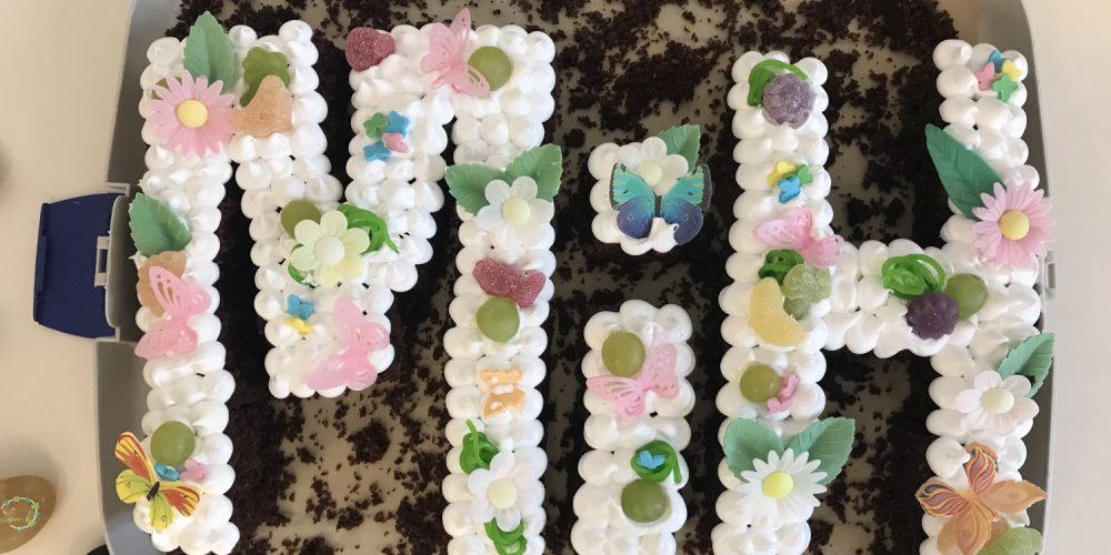 Ein Kuchen aus den Buchstaben M, i und H. Mit bunten Zuckerblumen dekoriert.