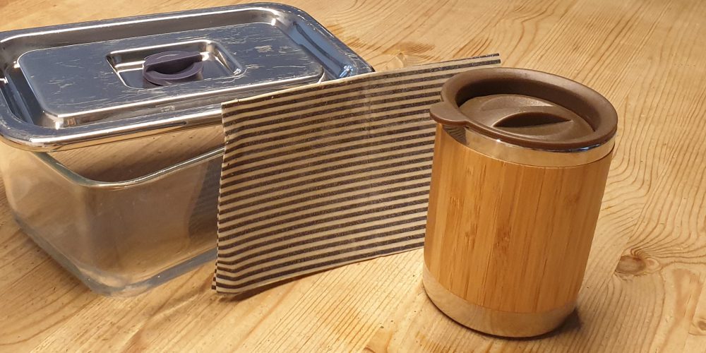 Zusehen sind 3 plastikfreie Verpackungs- bzw. Aufbewahrungsgegenstände, nämlich winw Glasbox mit Deckel, ein Bienenwachstuch und eine Tasse zum Mitnehmen aus Bambus mit Deckel