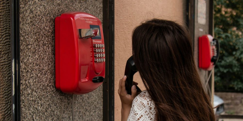 Frau mit braunen Haaren steht an rotem Telefon.