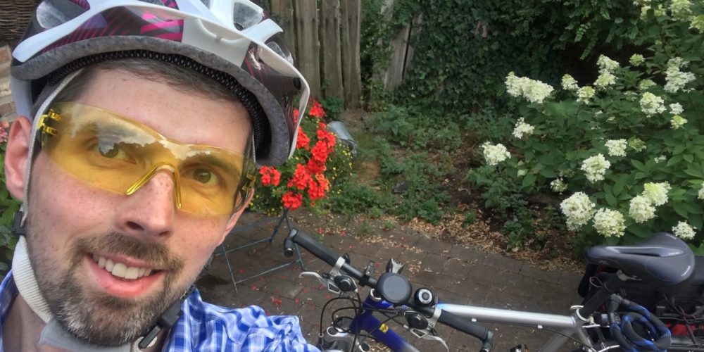 Daniel bereitet sich schon vor aufs Radeln: Hier steht er vor seinem Fahrrad mit Schutzhelm und Schutzbrille.