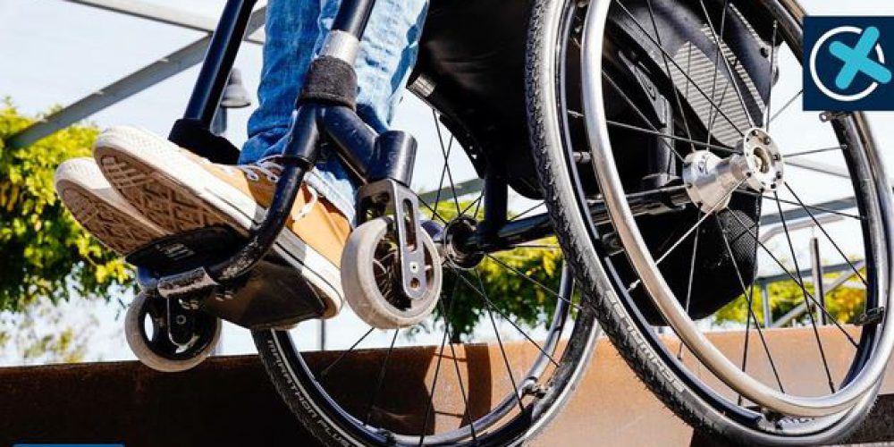 Von einem Rollstuhlfahrer sind nur die Füße , Waden und die Räder des Rollstuhls zu sehen.