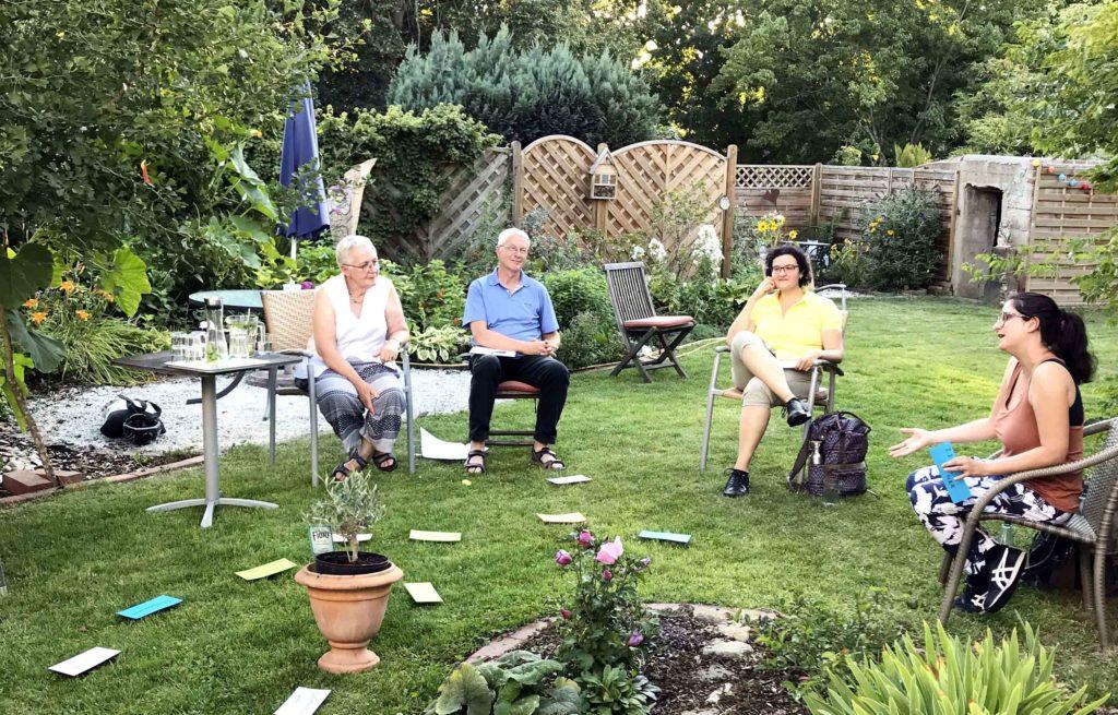 In einem Garten sitzen 4 Personen und diskutieren angeregt. Auf der Wiese liegen Karten, um das Thema Frauenquote zu veranschaulichen.