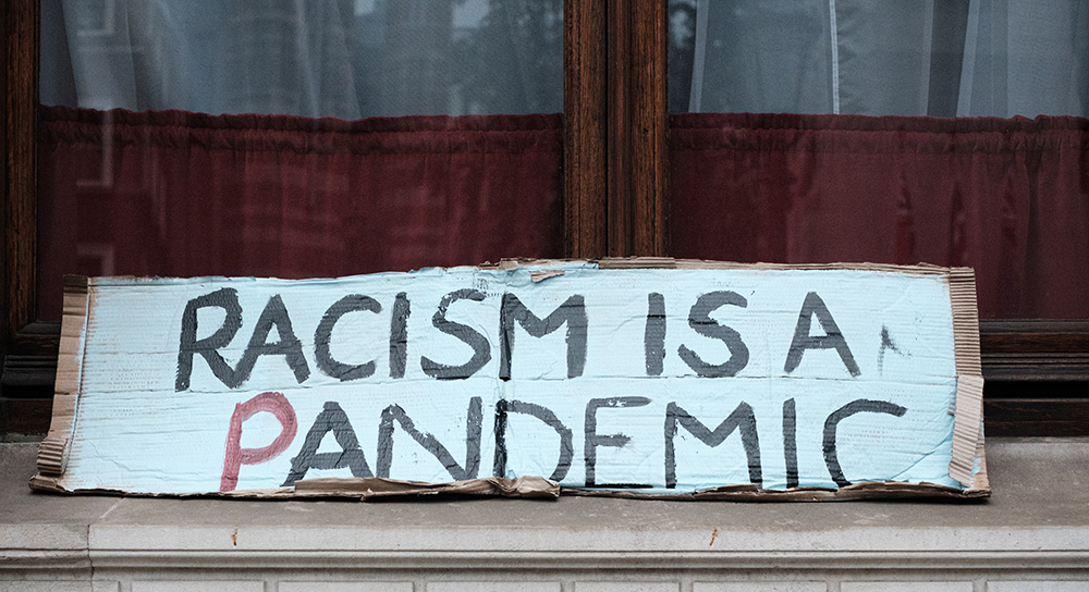 Ein Pappschild mit der Aufschrift: Racism is a pandemic - Übersetzung: Rassismus ist eine Pandemie.