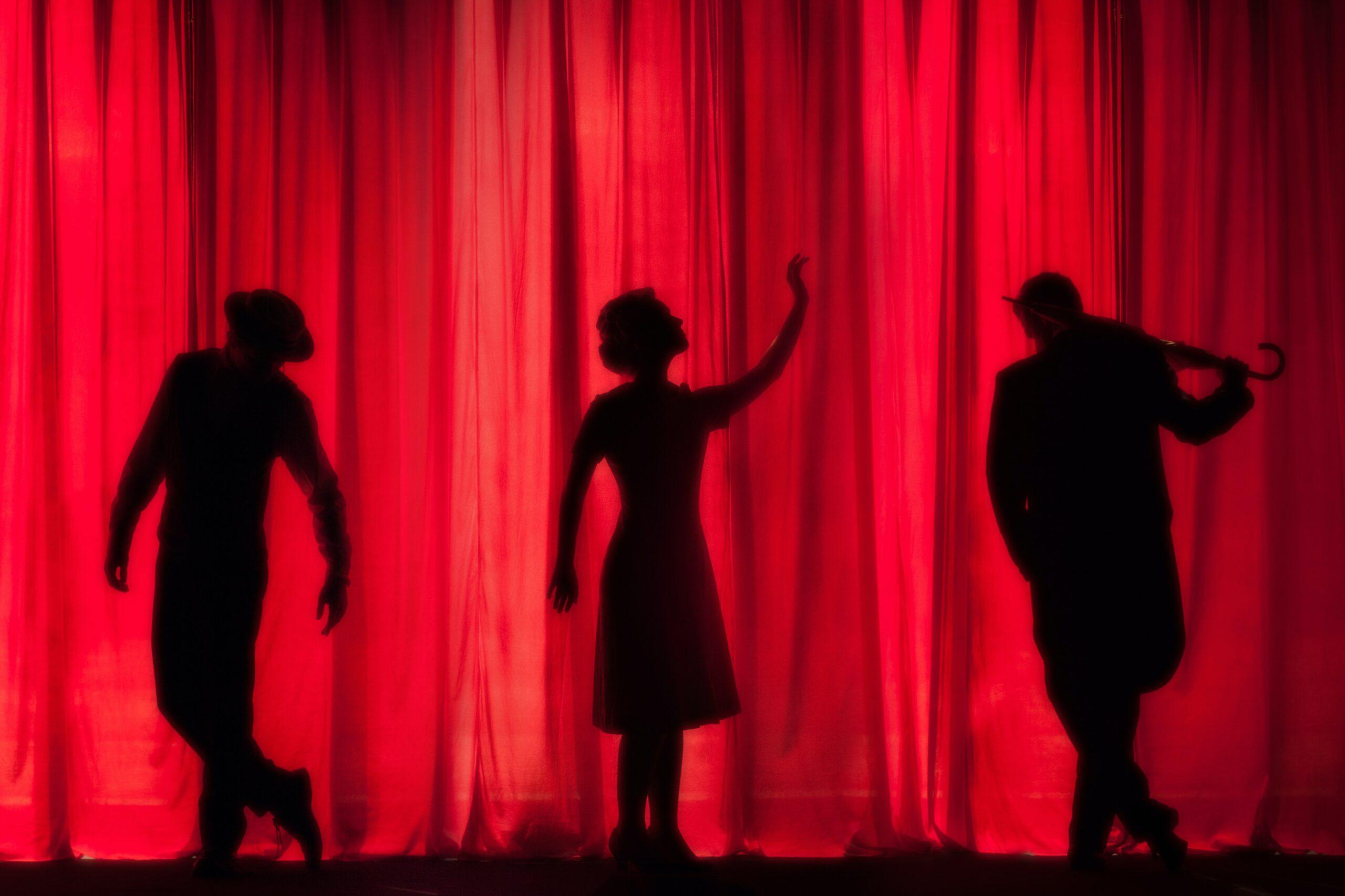 Es ist ein roter Theatervorhang mit den Schatten von 3 Schauspielern davor zusehen