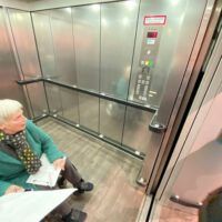 Eine Person im Rollstuhl befindet sich in einem großflächigen Aufzug und schaut in die erreichte Etage hinaein