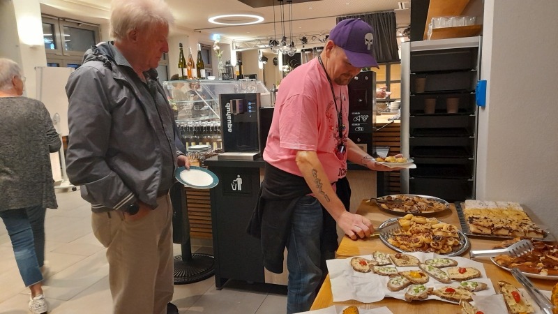 Ein Buffet-Tisch ist zu sehen, an den sich Menschen angestellt haben