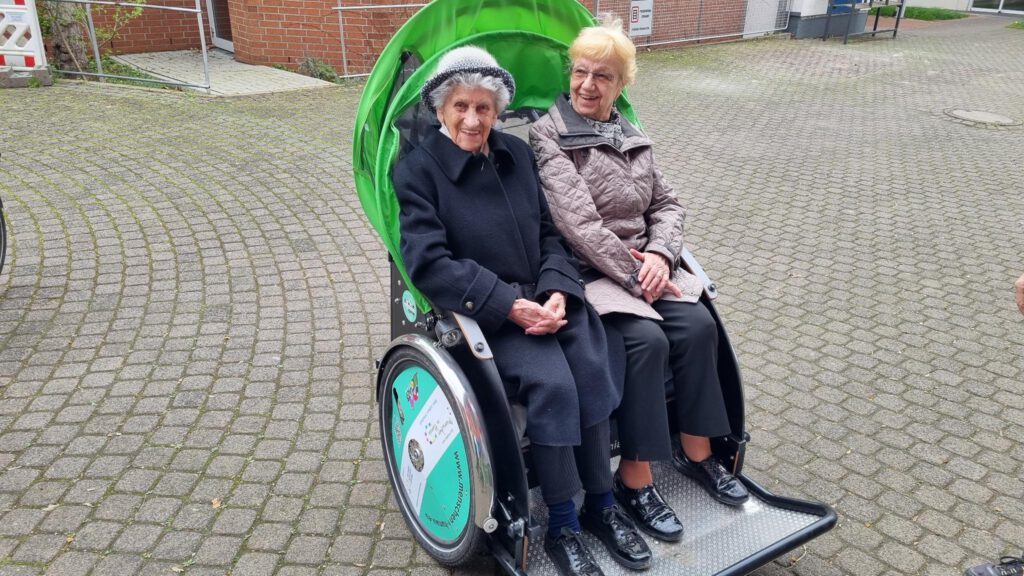 Eine Dame in schwarzer Jacke und eine in grauer in der RIkscha