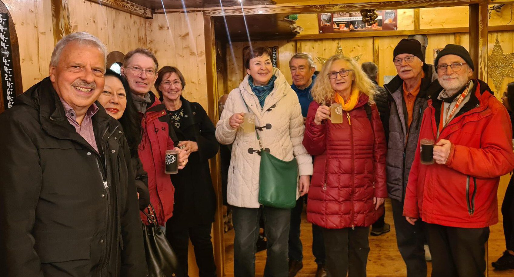 Mehrere Leute stehen zusammen und halten Glühweingläser hoch.