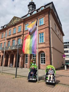 Zwei Rikschas mit Fahrgästen stehen vor dem Hanauer Rathaus, an dem eine Regenbogenfahne hängt.