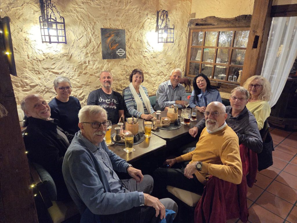 Das Rikscha-Team sitzt beim Stammtisch an einem langen Tisch in einem gemütlichen Restaurant und lächelt in die Kamera.