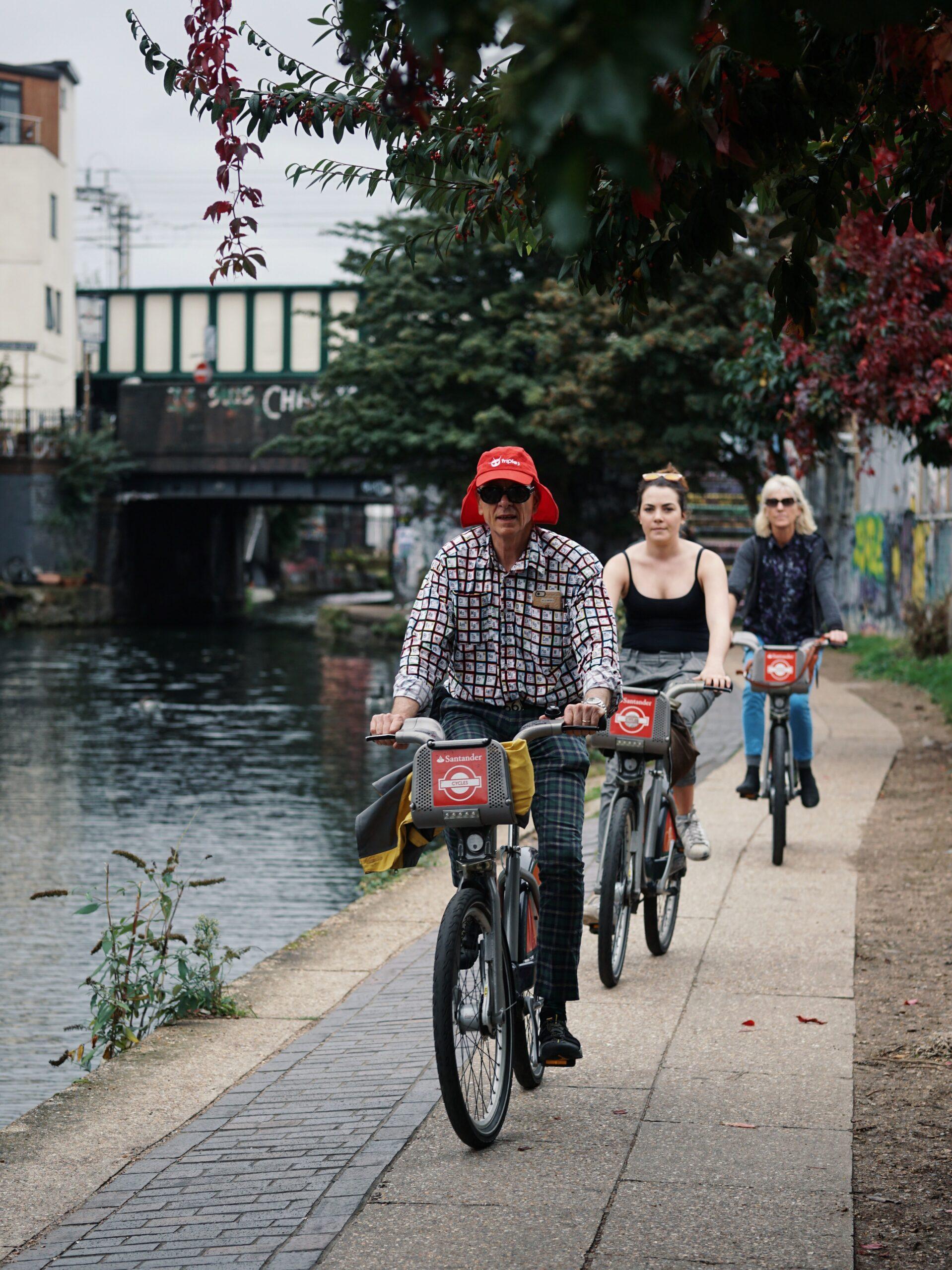 Es sind 3 Menschen auf Fahrrädern zu sehen die eine Fahrradtour entlang eines Kanals machen.